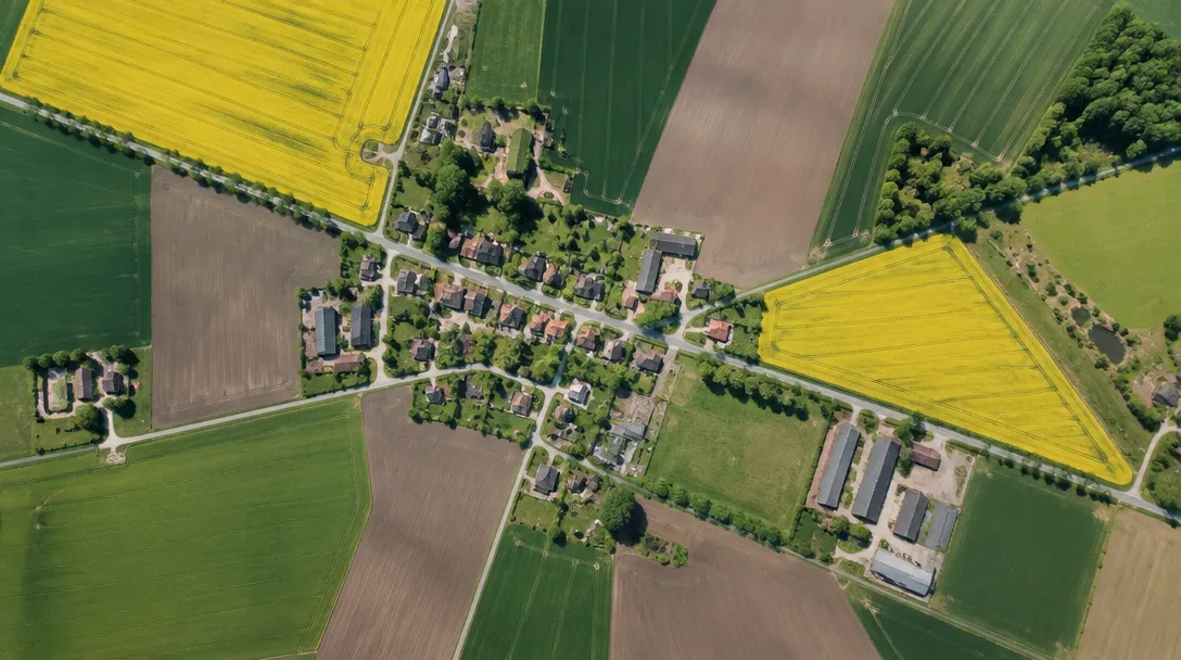 Flygfoto över slättlandskap med åkrar i olika färger och en liten by
